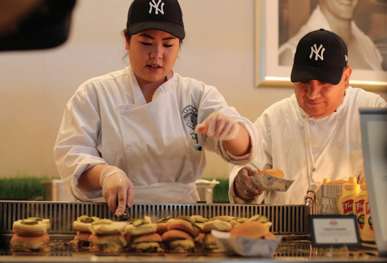 Man and woman, both in New York Yankees ball caps and white chefs coats, work at EVO EVent ventless griddle making sliders