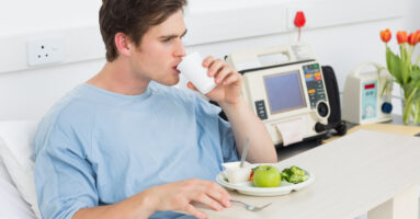 Young male patient drinking water while having meal in hospital