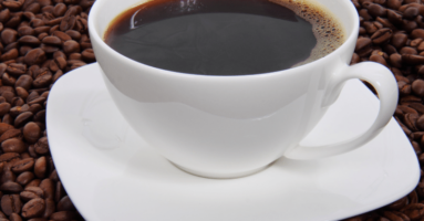 Coffee in white cup on white saucer sitting on bed of coffee beans