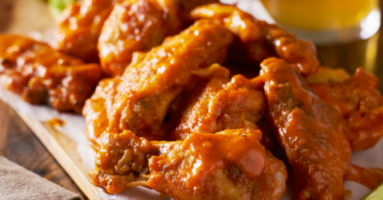 Chicken wings with sauce on top of white paper and wood platter with napkin in foreground