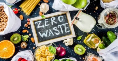 Chalkboard with 'zero waste' written on it surrounded by fruits, vegetables, pasta and other foods