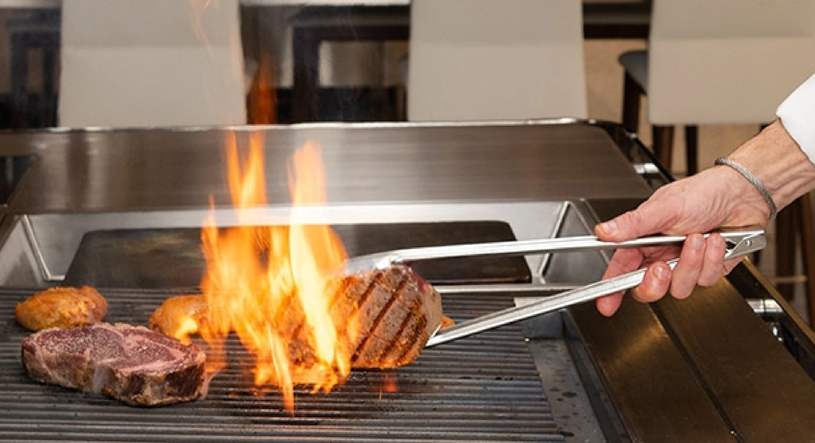 Flipping a steak on a charbroiler with flames