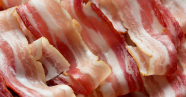 close up of uncooked strips of bacon ribboning across the screen